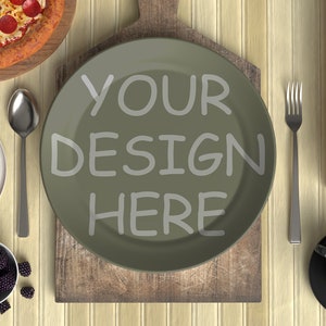 以下が含まれることがあります： 木製のまな板の上に置かれた緑色の皿に「YOUR DESIGN HERE」という文字が書かれています。皿の周りには、ピザ、ワッフル、ドーナツ、コーヒーなど、さまざまな食べ物があります。