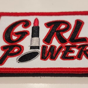 May include: Red and black embroidered patch with the text "GIRL POWER" and a red lipstick with a black cap and a silver base.