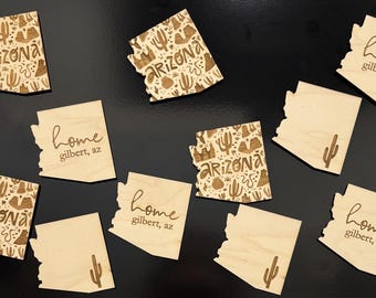 Puede incluir: Un conjunto de ocho imanes de madera con forma del estado de Arizona. Los imanes presentan una variedad de diseños, que incluyen un cactus, una cordillera y las palabras "home" y "gilbert, az".