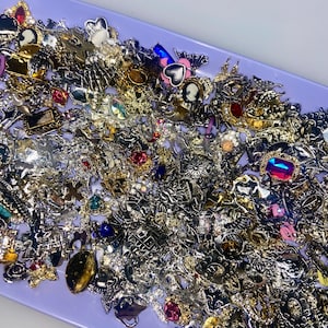 May include: A tray filled with a variety of silver and gold-toned charms, including hearts, flowers, and other decorative designs. Some charms have colourful gemstones, such as red, blue, and green.
