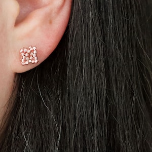 Op de afbeelding: Een paar vierkante oorbel studs van roségoud. De oorbel studs zijn gemaakt van kleine, vierkante kralen die bij elkaar zijn geclusterd om een vierkante vorm te creëren.