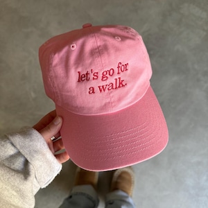 May include: Pink baseball cap with the text "Let's go for a walk." embroidered in red.