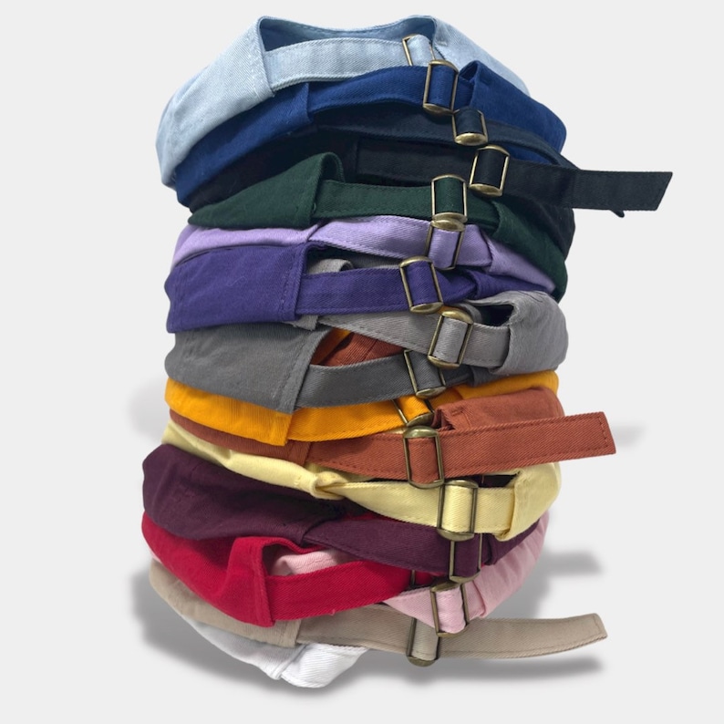 May include: A stack of 12 baseball caps in various colors, including blue, green, purple, gray, yellow, orange, maroon, red, pink, beige, and white. Each cap has a buckle closure.
