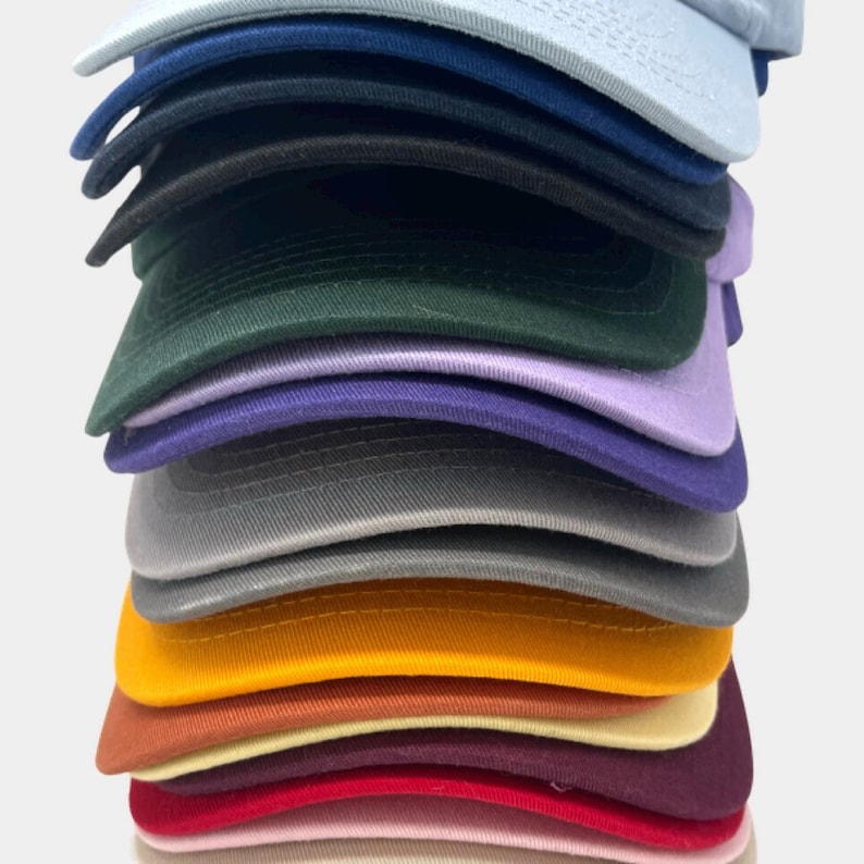 May include: A stack of 15 plain baseball caps in various colors, including light blue, dark blue, black, green, purple, gray, yellow, orange, brown, red, pink, and white.