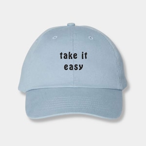 May include: A light blue baseball cap with the words "take it easy" in black block letters. The cap has a curved brim and a rounded crown. The hat is made of a soft, durable fabric.