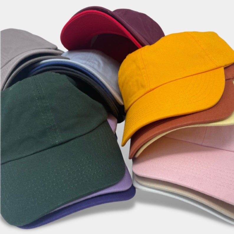 May include: A stack of plain baseball caps in various colors, including red, purple, yellow, green, gray, blue, pink, beige, and white.