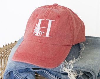 May include: A red baseball cap with a white embroidered letter "H" and floral design. The cap has a curved brim and a distressed look.