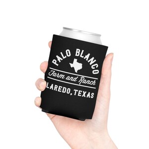 May include: Black neoprene can cooler with white text that reads "Palo Blanco Farm and Ranch Laredo, Texas". The cooler features a white outline of the state of Texas.