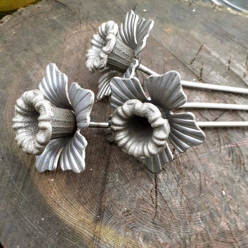 Puede incluir: Tres candelabros de metal plateado en forma de flor con una superficie texturizada. Los candelabros est&aacute;n sobre una superficie de madera.