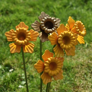 Puede incluir: Cinco esculturas de flores de metal en tonos amarillos y marrones. Las flores tienen un dise&ntilde;o fruncido y en capas y est&aacute;n unidas a tallos de metal.