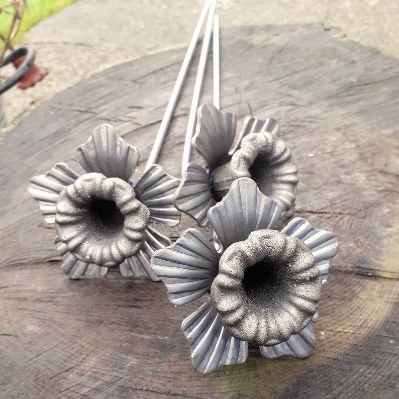 Puede incluir: Tres flores de metal con tallos largos. Las flores son plateadas y tienen un dise&ntilde;o detallado. Las flores est&aacute;n dispuestas en un ramo.