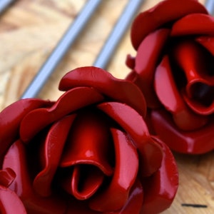 May include: Two red metal roses with a shiny finish. The roses are made of metal and have a realistic appearance.