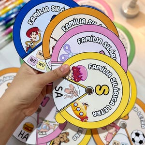 Puede incluir: Un conjunto de ayudas de aprendizaje circulares y coloridas para niños. Cada rueda presenta una letra diferente del alfabeto y sílabas correspondientes. Las ruedas están etiquetadas "Familia Silabica" y "Letra".