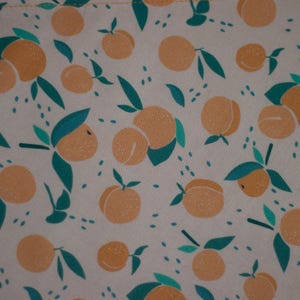 May include: A beige fabric with a repeating pattern of orange fruit and green leaves. The fruit is stylized and resembles oranges or peaches.