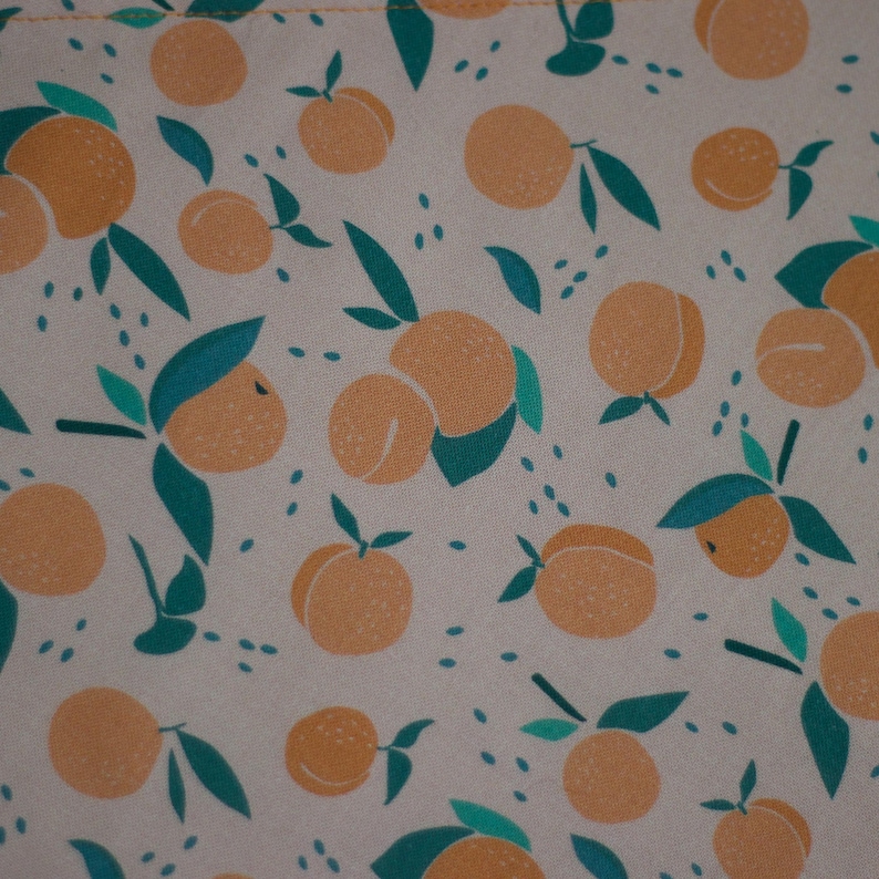May include: A beige fabric with a repeating pattern of orange fruit and green leaves. The fruit is stylized and resembles oranges or peaches.