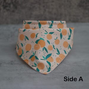 May include: A peach-colored bandana with a pattern of green leaves and orange peaches. The bandana is folded in a triangular shape and the text "Side A" is printed on the bottom right corner.