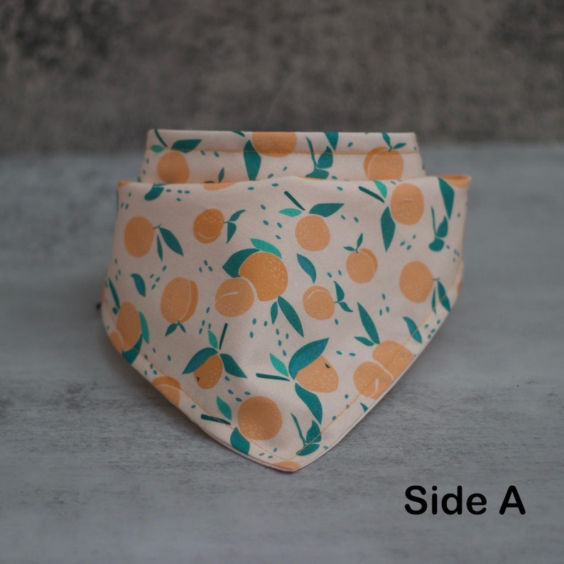 May include: A peach-colored bandana with a pattern of green leaves and orange peaches. The bandana is folded in a triangular shape and the text "Side A" is printed on the bottom right corner.