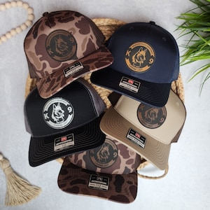 May include: Five different baseball caps with a K9 patch on the front. The caps are in various camouflage patterns, black, and tan. The patches feature a German Shepherd dog and the text "K9 Canine Unit".
