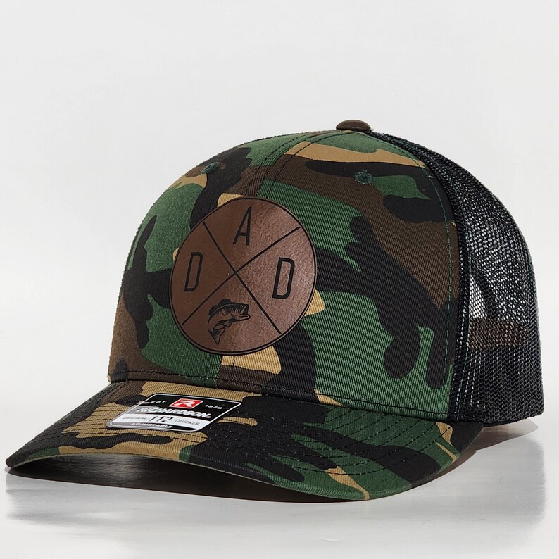 May include: A camouflage trucker hat with a brown leather patch that says "DAD" with a fish graphic inside the letters.
