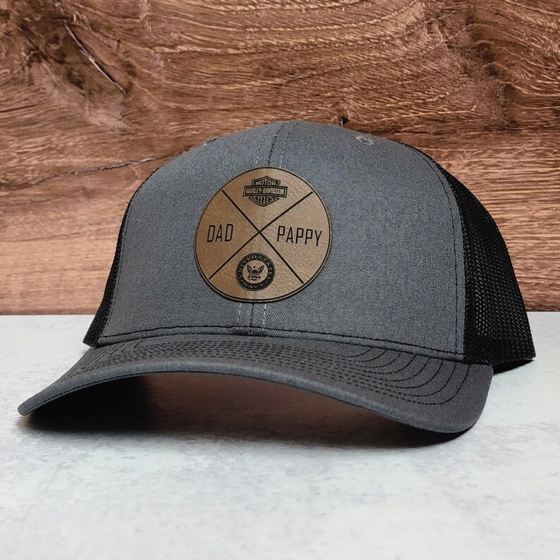 May include: A gray and black trucker hat with a brown leather patch that says "DAD" and "PAPPY" with a Harley Davidson logo in the center.