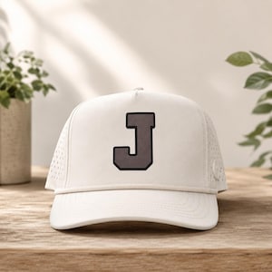 May include: A white baseball cap featuring a large, dark gray letter J patch on the front panel. The cap includes a matching white rope detail across the base of the crown and perforated side panels for ventilation, constructed with a structured design.