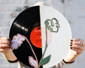 May include: A black and white vinyl record painted with a green and gold leaf design. The record is split in half, with one side painted black and the other side painted white. The leaf design is painted on both sides of the record.