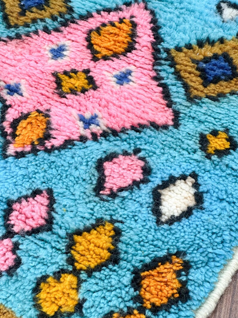 K&ouml;nnte beinhalten: Nahaufnahme eines bunten, strukturierten Teppichs mit geometrischem Muster. Der Teppich zeigt Farbt&ouml;ne von Blau, Rosa, Gelb und Braun.