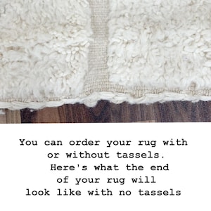 May include: Close-up of a cream-colored rug with a shaggy texture and a woven border. The rug's edge is visible, showing a detailed fringe. The text on the image says, "You can order your rug with or without tassels. Here's what the end of your rug will look like with no tassels."