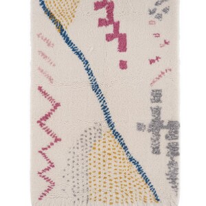 K&ouml;nnte beinhalten: Cremefarbener rechteckiger Teppich mit geometrischem Design. Er hat eine blaue Diagonallinie, rosa Zickzackmuster und gelbe und graue gepunktete Muster. Der Teppich hat einen Fransenrand, der Textur und visuelles Interesse verleiht.