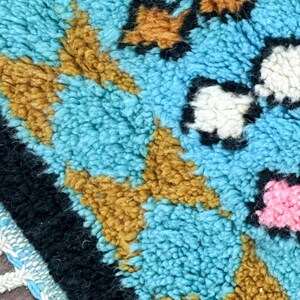 K&ouml;nnte beinhalten: Nahaufnahme eines blauen, braunen, wei&szlig;en und rosafarbenen Teppichs mit Muster und Fransenrand. Der Teppich besteht aus einem weichen, flauschigen Material.