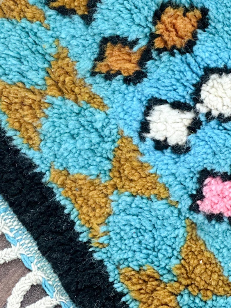 K&ouml;nnte beinhalten: Nahaufnahme eines blauen, braunen, wei&szlig;en und rosafarbenen Teppichs mit Muster und Fransenrand. Der Teppich besteht aus einem weichen, flauschigen Material.