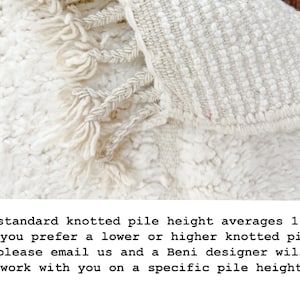 May include: Close-up of a cream-colored rug with a textured, knotted pile and fringe detailing. The rug's pile height averages 1.25 inches. The rug has a soft, inviting appearance, suitable for home decor.