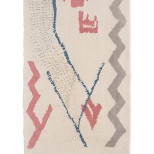 May include: Cream-colored rectangular rug with a geometric design. Features pink, blue, and gray shapes, including zigzags and arrows. The rug has a fringed edge and a textured surface, suitable for home decor.