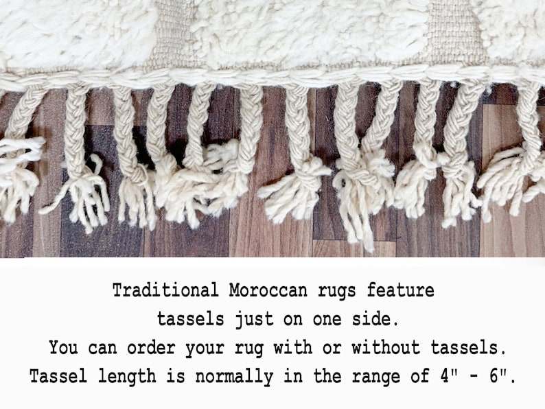 May include: Close-up of a cream-colored rug with a textured weave and knotted fringe tassels. The tassels are approximately 4 to 6 inches long. The rug is a traditional Moroccan style.