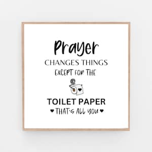 Op de afbeelding: Een wit bord met een zwarte rand en de tekst "Gebed verandert dingen behalve voor toiletpapier Dat is alles wat je hebt" met een cartoonafbeelding van een toiletpapierrol.