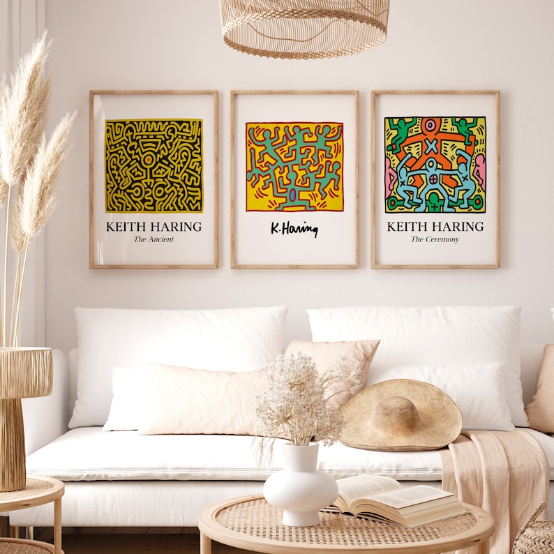 May include: Three framed prints of Keith Haring artwork. The prints are in a minimalist style with a white background and black frames. The artwork features colorful figures and abstract designs. The titles of the prints are "The Ancient", "K. Haring", and "The Ceremony".