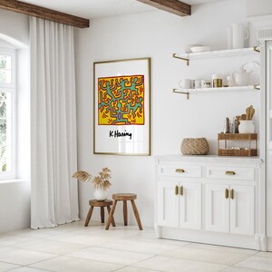 May include: A framed print of a colorful abstract art piece by artist K. Haring. The artwork features a yellow background with green, red, and blue figures.