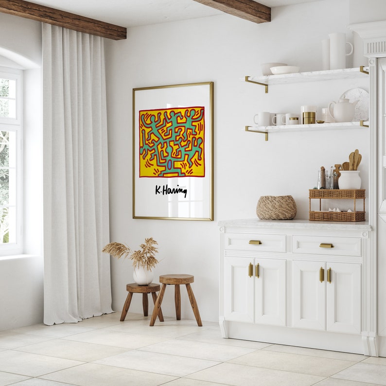 May include: A framed print of a colorful abstract art piece by artist K. Haring. The artwork features a yellow background with green, red, and blue figures.