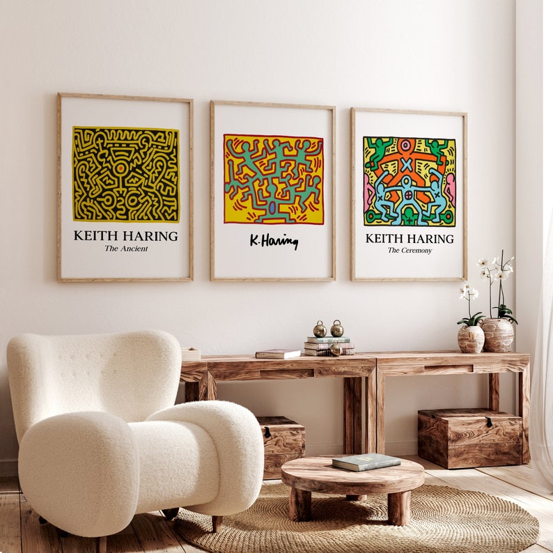 May include: Three framed prints of Keith Haring artwork. The prints are in a living room setting with a white armchair, a wooden coffee table, and a wooden console table. The prints are titled "The Ancient", "K. Haring", and "The Ceremony".