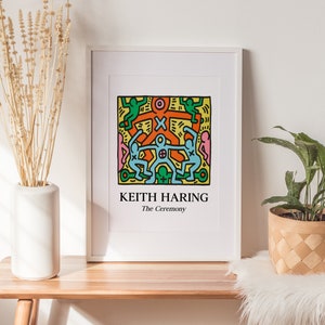 May include: A white framed print of a Keith Haring artwork titled "The Ceremony". The artwork features a colorful illustration of stick figures in a circle, with a yellow background.