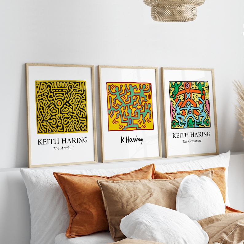 May include: Three framed prints of Keith Haring artwork. The prints are in a minimalist style with black frames and white mats. The artwork features colorful figures and abstract designs. The titles of the prints are "The Ancient", "K. Haring", and "The Ceremony".