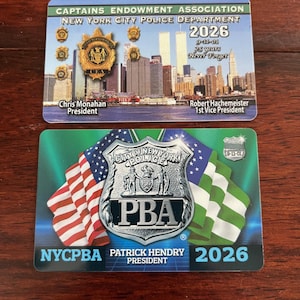 May include: Two New York City Police Department ID cards. The top card features a skyline with the Twin Towers and the text "2026" and "9-11-01 25 years Never Forget". The bottom card has the text "PBA" and "2026" with flags.