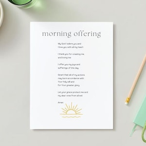 May include: A white paper with the words "morning offering" and a prayer printed in black. A pencil, a small green notebook, and a set of keys are on the right. A bowl of grapes is in the upper left.
