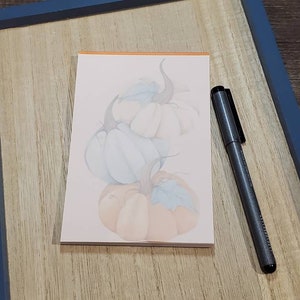 May include: A stack of three pastel-colored pumpkins with a light orange stem on top. The pumpkins are painted in shades of blue and peach.