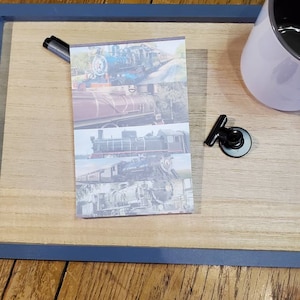 May include: A close-up of a notepad with a collage of vintage train images. The notepad is on a wooden surface with a mug and a paperclip.