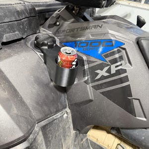 May include: A black cup holder attached to a gray ATV. A red and white can of soda is in the cup holder. The ATV has the word "Sportsman" and "1000 EFI" printed on it.