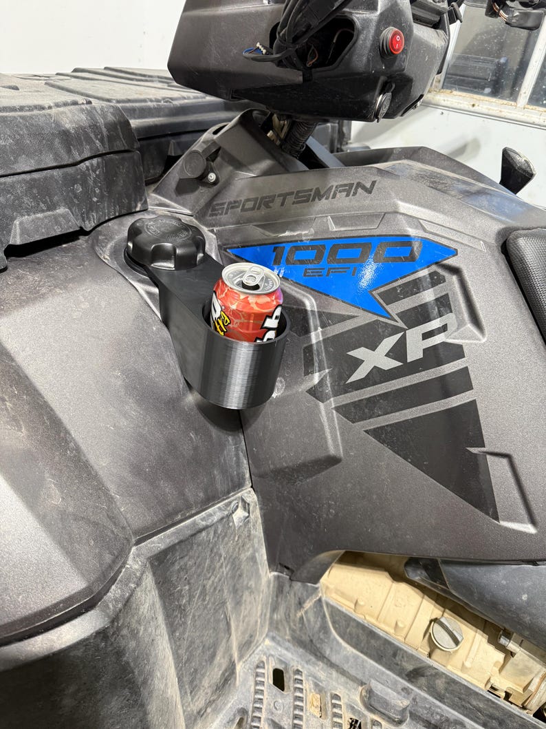 May include: A black cup holder attached to a gray ATV. A red and white can of soda is in the cup holder. The ATV has the word "Sportsman" and "1000 EFI" printed on it.