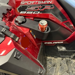 May include: A red and black Polaris Sportsman SP 850 HD ATV with a cup holder containing a can of soda. The ATV has the word "SPORTSMAN" printed on the side in white lettering.