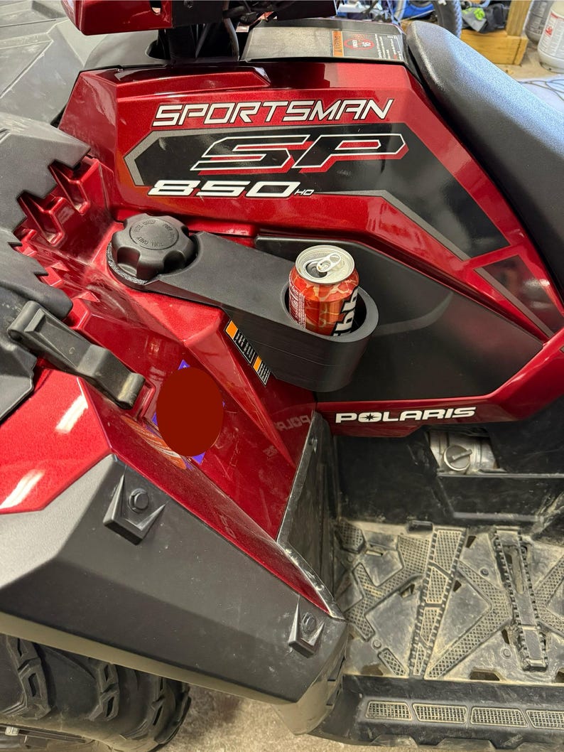 May include: A red and black Polaris Sportsman SP 850 HD ATV with a cup holder containing a can of soda. The ATV has the word "SPORTSMAN" printed on the side in white lettering.