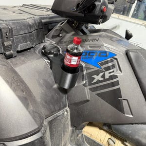 May include: A black 3D-printed cup holder attached to a gray ATV. A small bottle of Dr. Pepper is in the cup holder. The ATV has the words "SPORTSMAN 1000 XP" in blue and white.